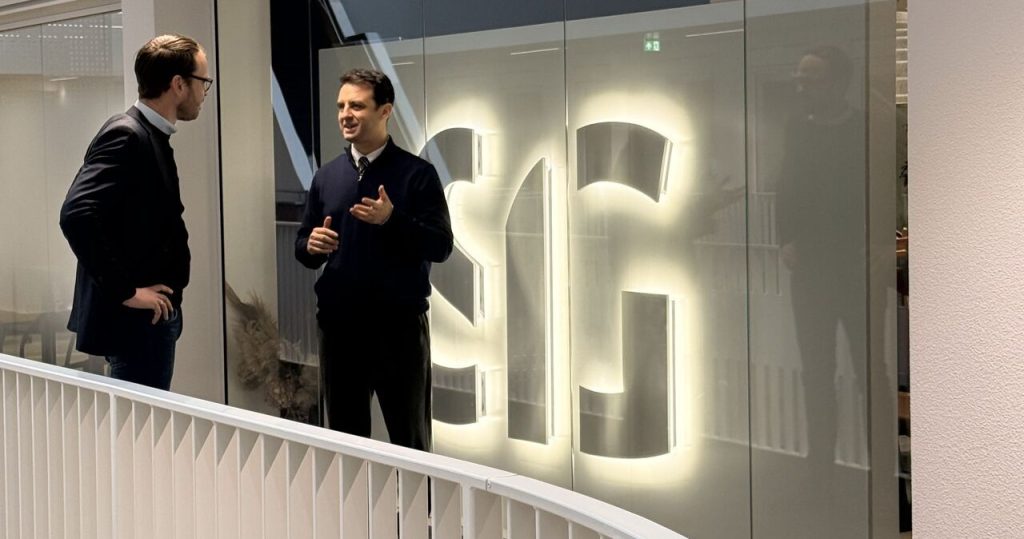 Two people conversing in front of Software Improvement Group office with illuminated letters displaying SIG.