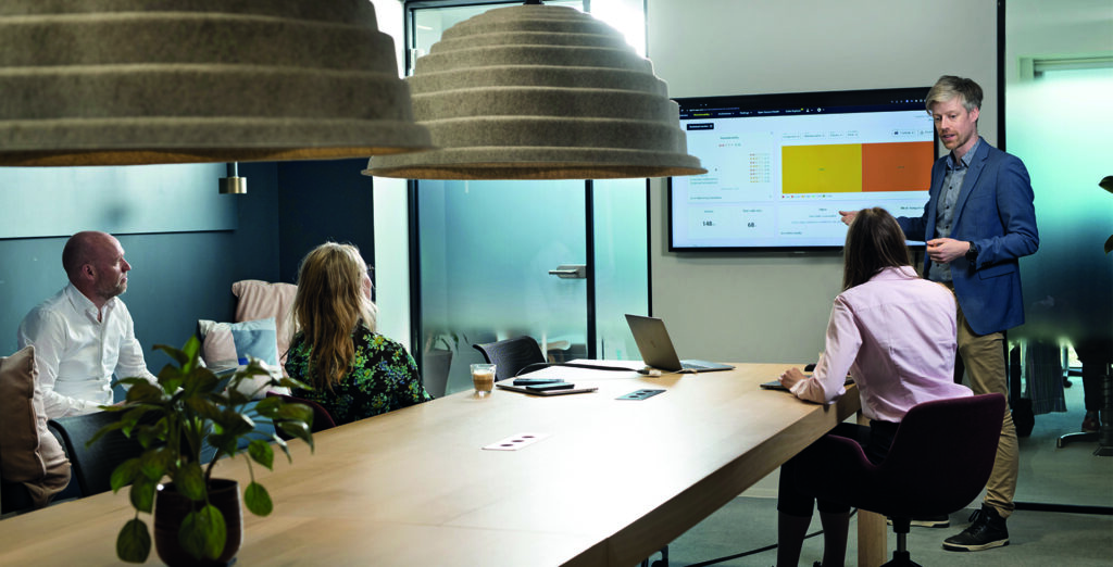 Image of team meeting in a modern conference room, with a presenter sharing data on a screen.
