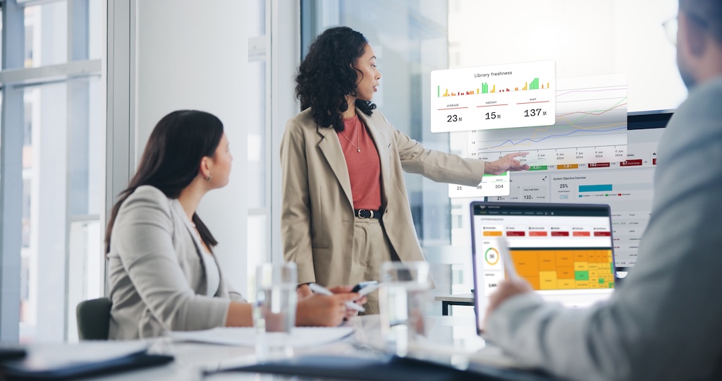 This is a mockup of a woman presents code quality datas on a screen to colleagues in an office meeting.