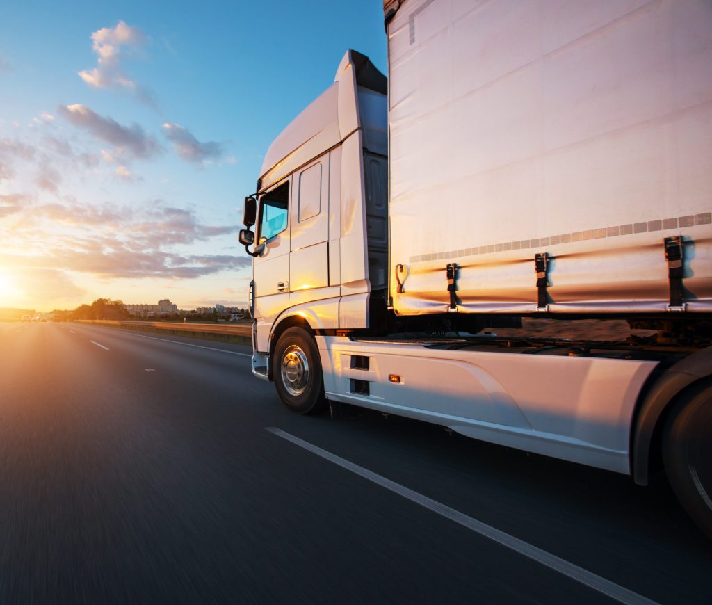 White semi-truck driving on a highway during sunset.