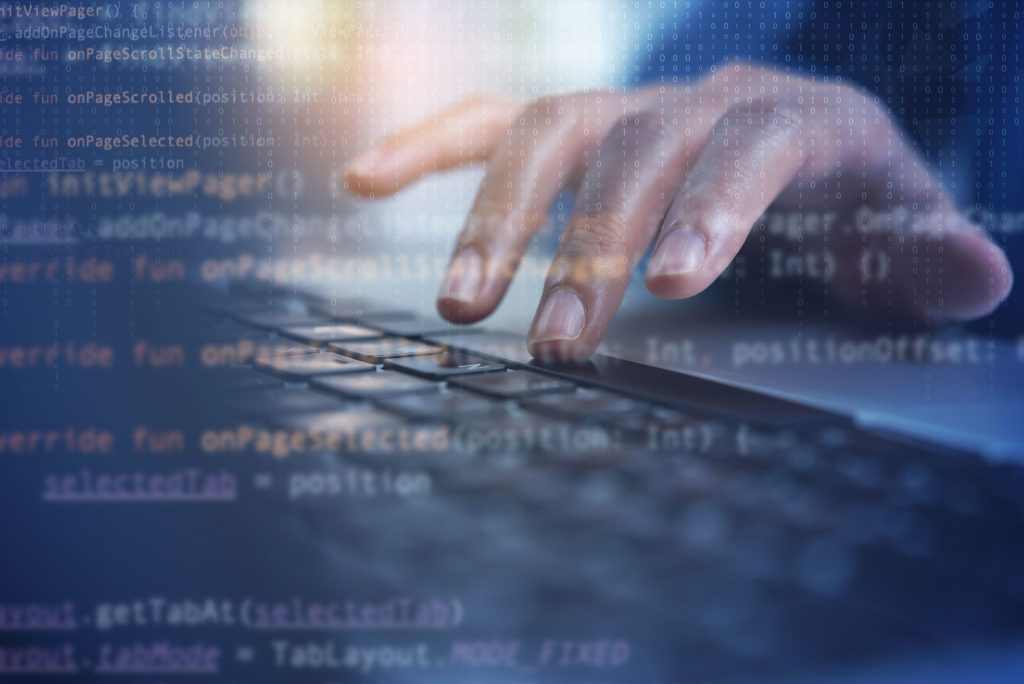 A hand typing on a laptop keyboard overlaid with semi-transparent code.