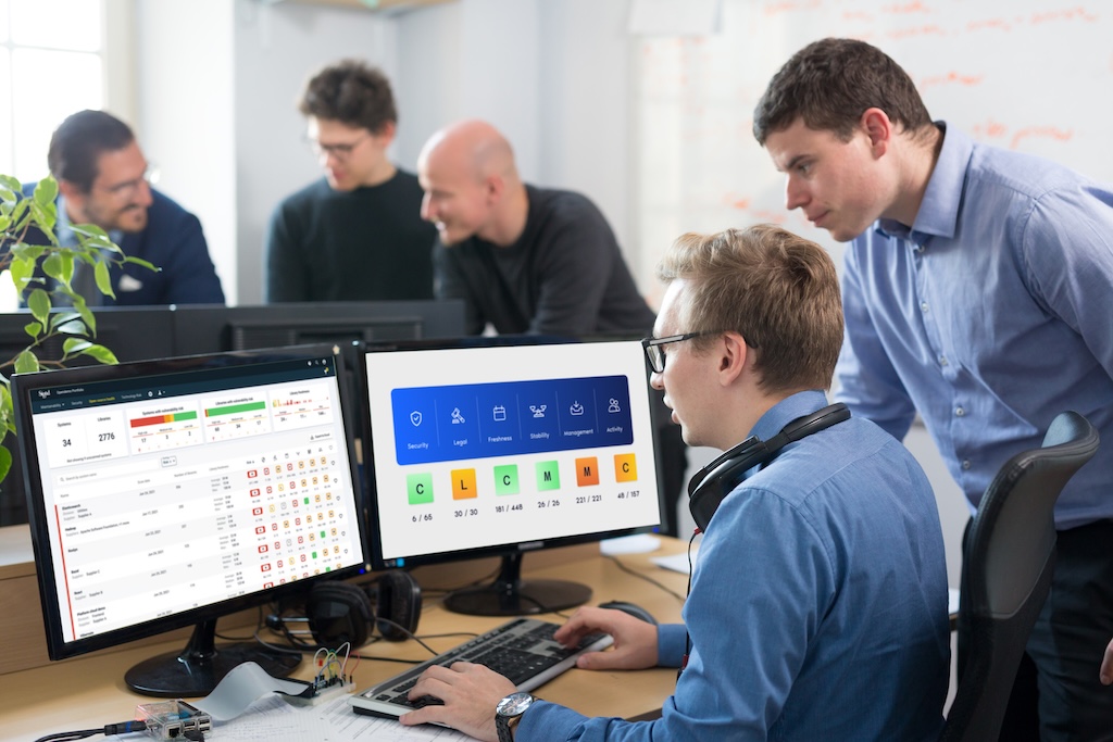 A group of people in an office reviewing data of Sigrid's feature of Open source Health on computer monitors.