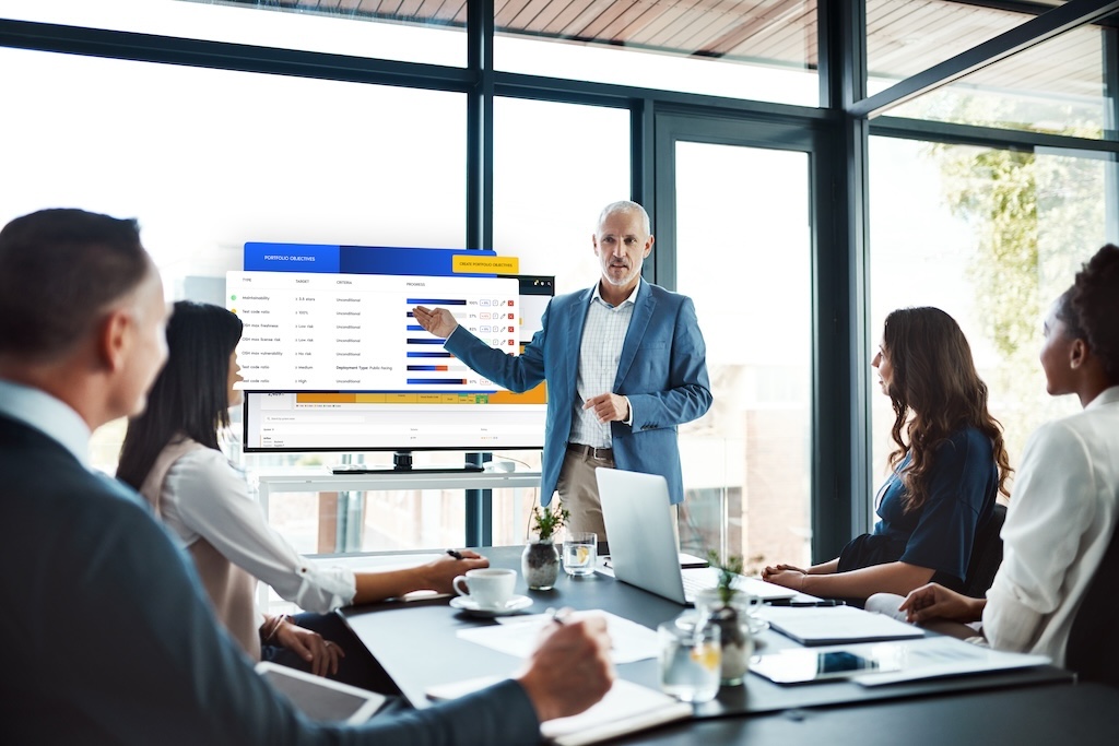 This is a mockup image of A business meeting with a man presenting Sigrid's feature of portfolio objectives on a screen to four seated colleagues.