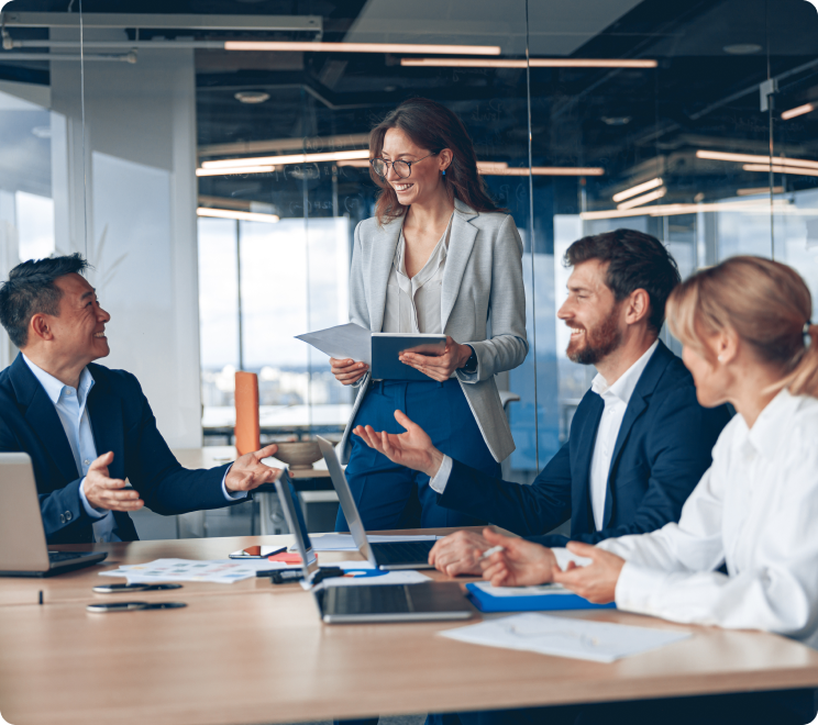 People in a business setting, sitting around a table and smiling while reading reports and discussing.