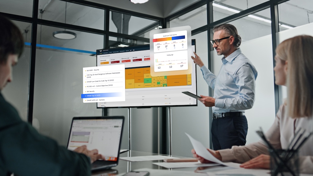 This is a mockup image of a man gives a presentation on a large screen in a modern office, with two colleagues seated at a table.