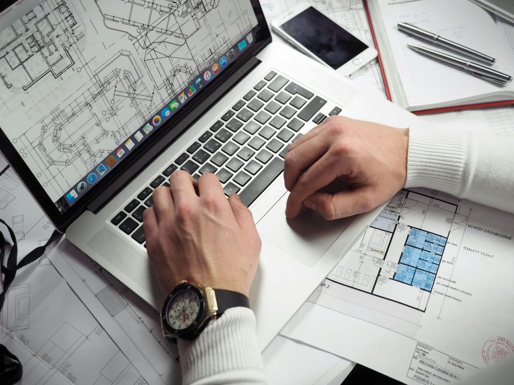 Image of a person using a laptop with architectural blueprints spread around.