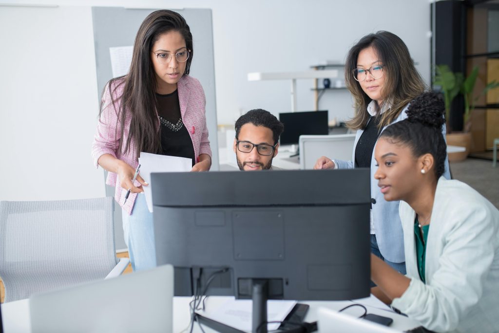 Four people looking together at a computer screen.