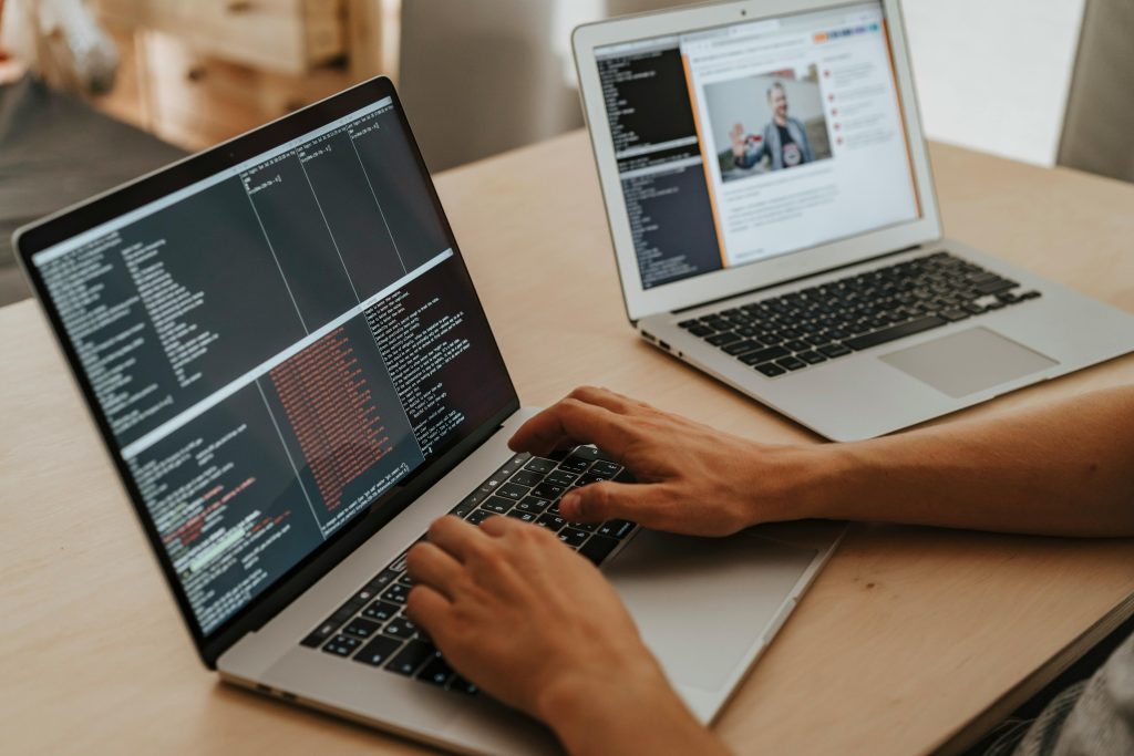Two laptops on a desk, one displays code and the other a webpage with an image of a person.