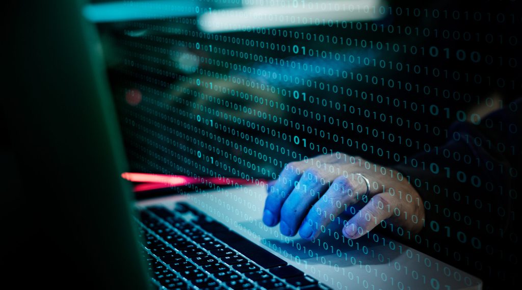 Visual of a hand typing on a laptop keyboard with binary code overlay.