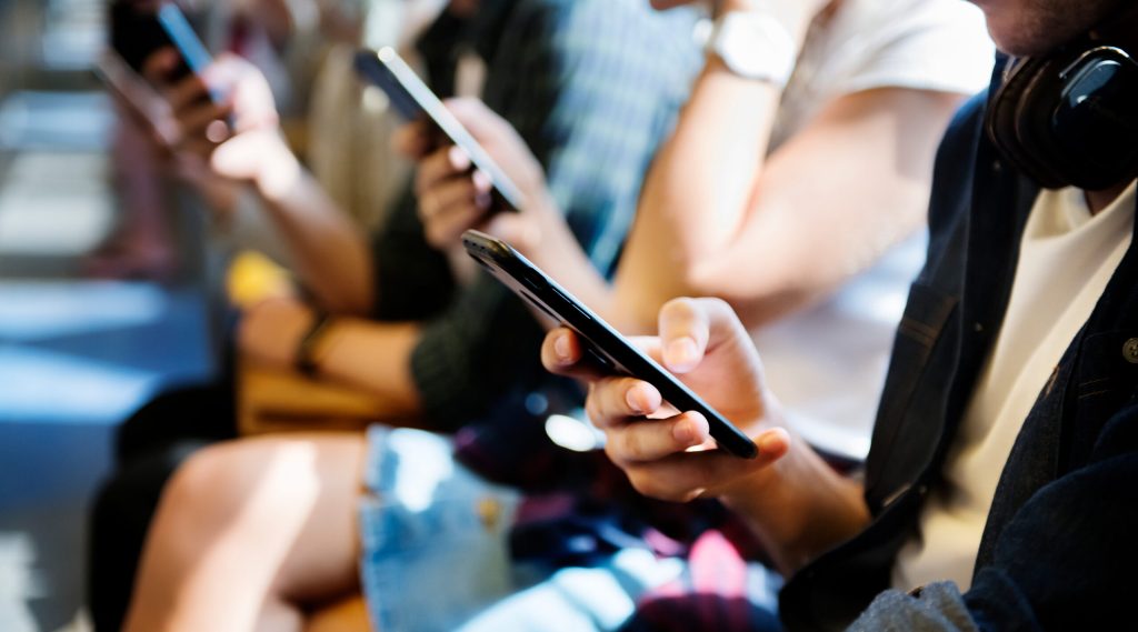Image of people seated, using smartphones, with focus on hands and devices.